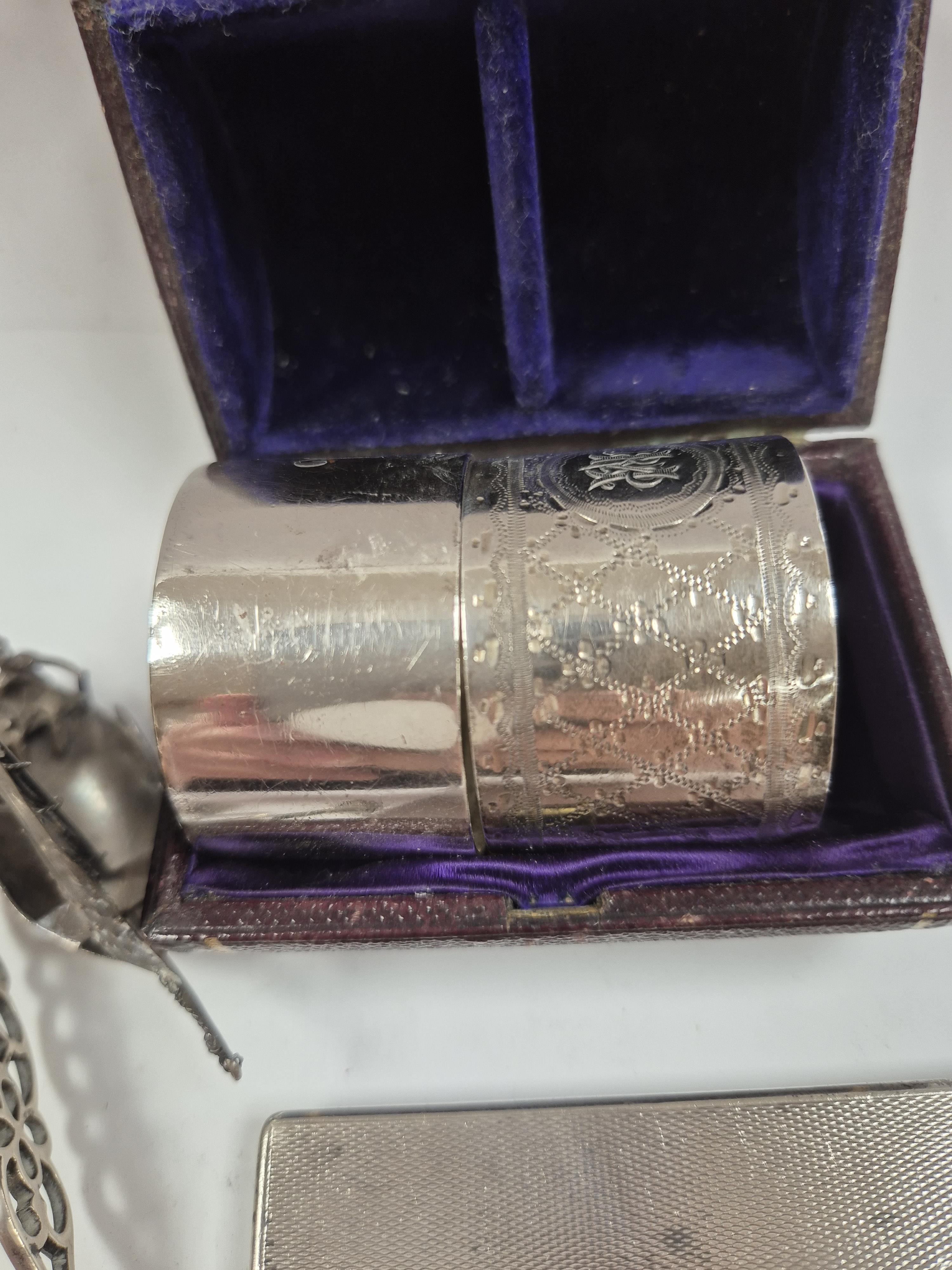 A 1930's engine turned silver cigarette case, 88mm, two silver napkin rings, a white metal miniature model of a boat and a pair of Georgian silver sugar tongs (a.f.). Condition - poor to fair